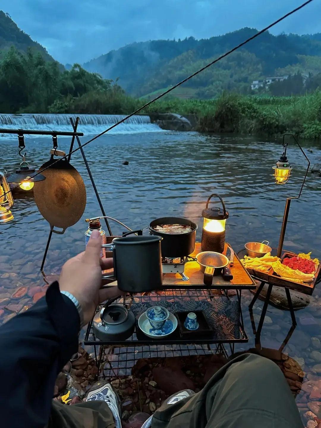 Outdoor dining setup by a river with lanterns, food, and drinks seen in ’People often go to places without ceilings.’