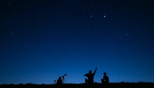 Silhouettes of people stargazing with a telescope under a dark sky filled with celestial objects.