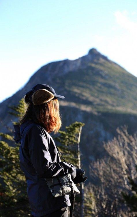 Hiker wearing a cap and jacket, facing a mountain peak, traverse uncharted territories.